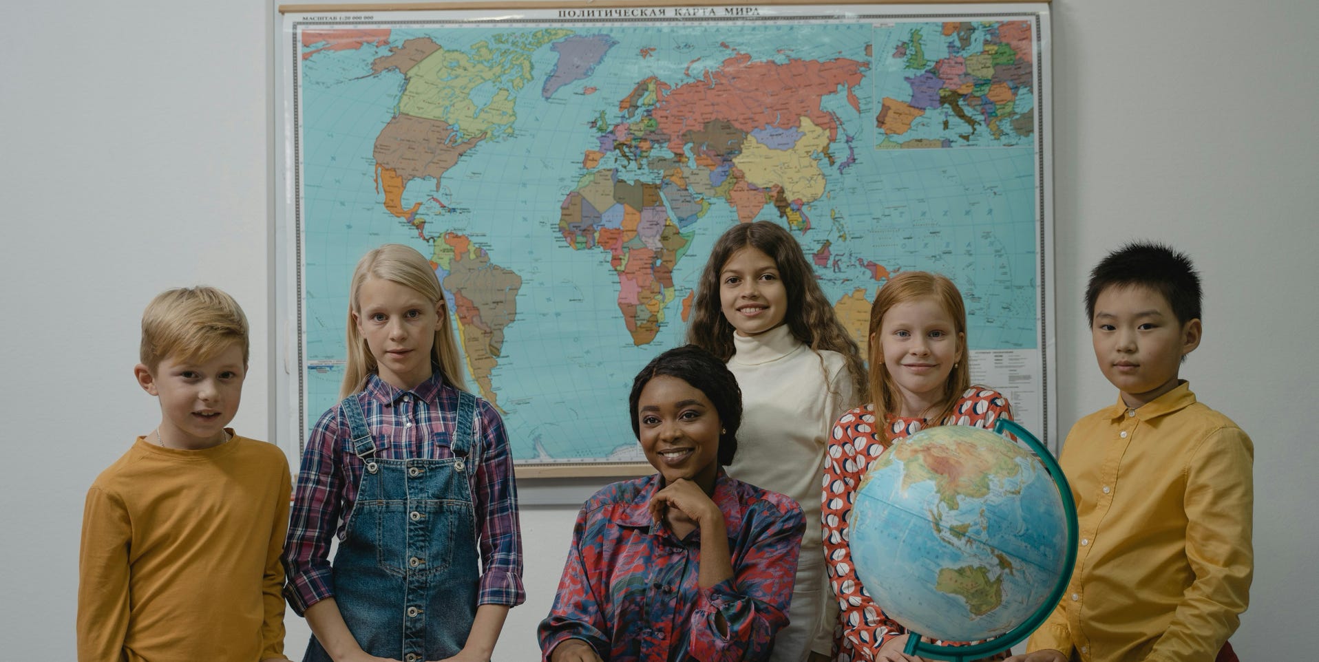 A diverse group of students with a teacher in a classroom setting featuring a globe and world map.