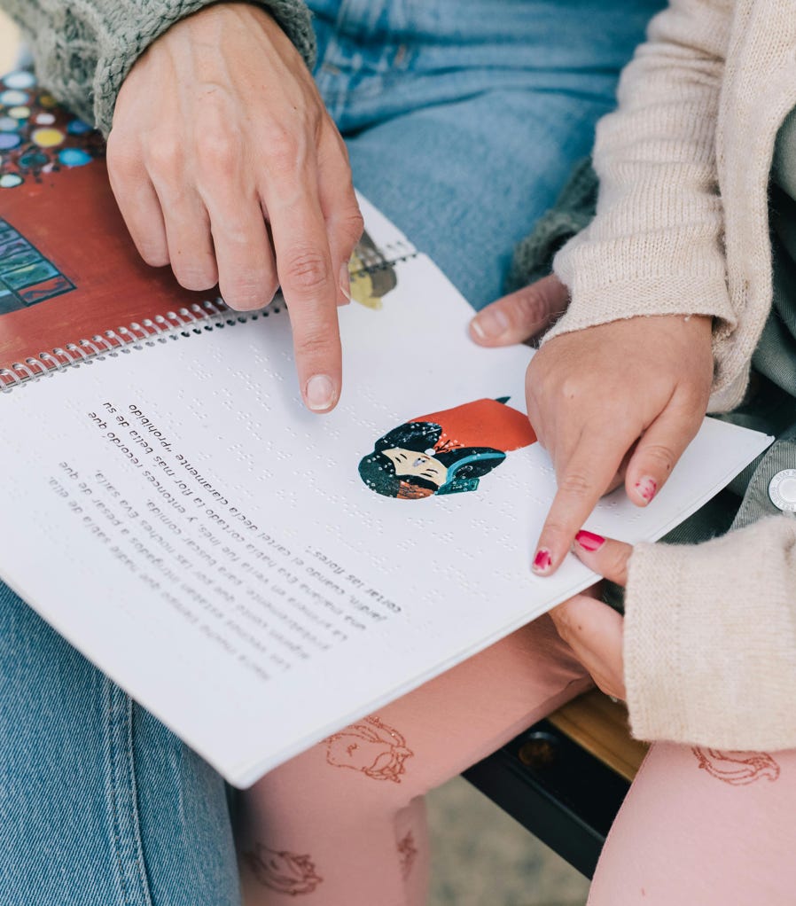 A mother and child enjoy reading a Braille storybook together outdoors, fostering bonding and learning.